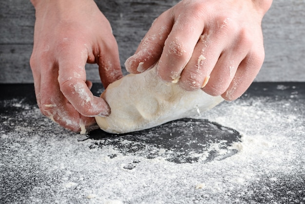 Hands knead the dough on a wooden table