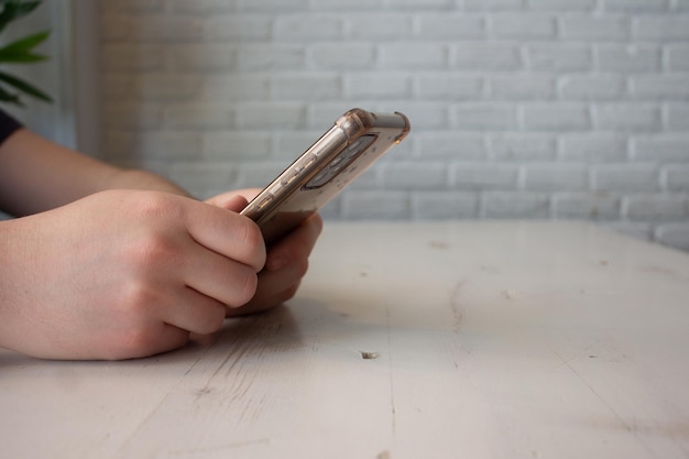 Hands leaning on white wooden table holding cell phone