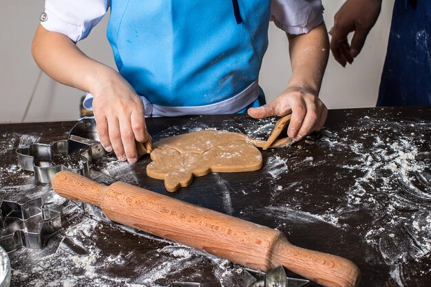 Hands of little girl sheeting dough with rolling pin. 