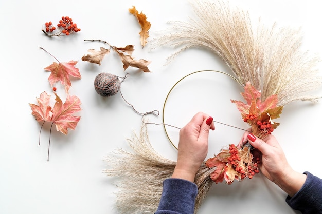 Hands making dried floral wreath from dry pampas grass and Autumn leaves Hands in sweater tie decorations to metal frame