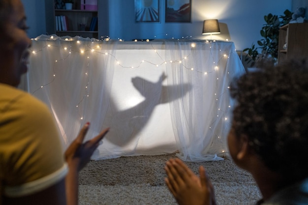 Hands making hand shadow of bird while performing playbehind white cloth against light