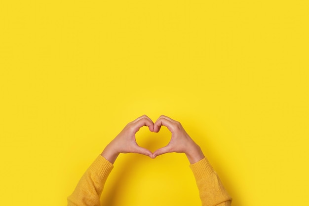 Photo hands making heart shape, love symbol over yellow background