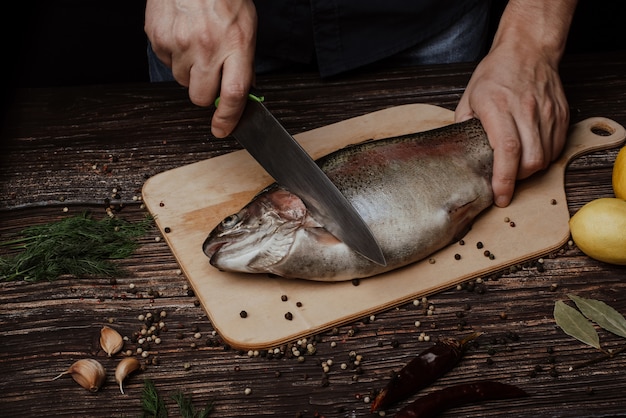 Hands of a male chef carving trout on a wooden table in the kitchen