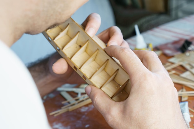 Hands of man gluing plywood details for ship model with glue holding with fingers Process of building toy ship