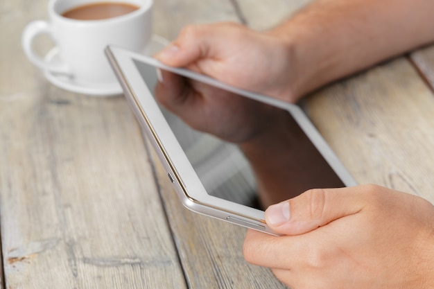 Hands of a man holding blank tablet device over a wooden workspace table