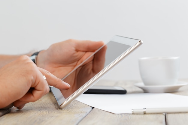 Hands of a man holding tablet device over a wooden workspace table