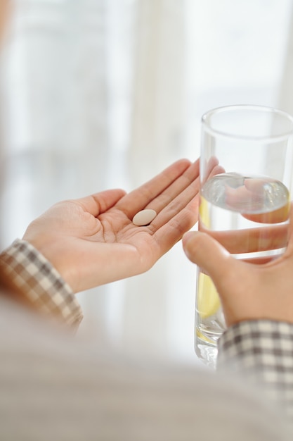 Hands of man taking painkiller and drinking glass of water