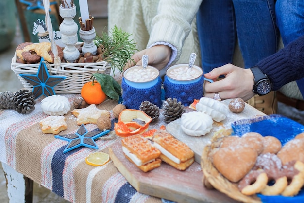 Hands of man and woman holding mugs with warm drink on table with winter decor