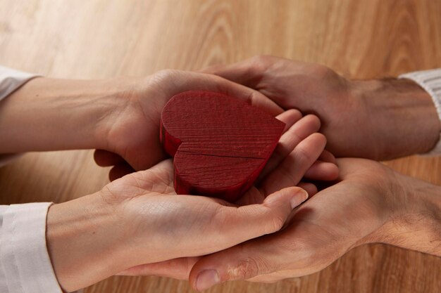 Hands of man and woman holding red heart protecting it together