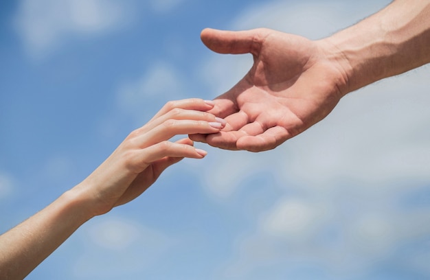 Hands of man and woman reaching to each other, support. Solidarity, compassion, and charity, rescue. Giving a helping hand. Hands of man and woman on blue sky background. Lending a helping hand.