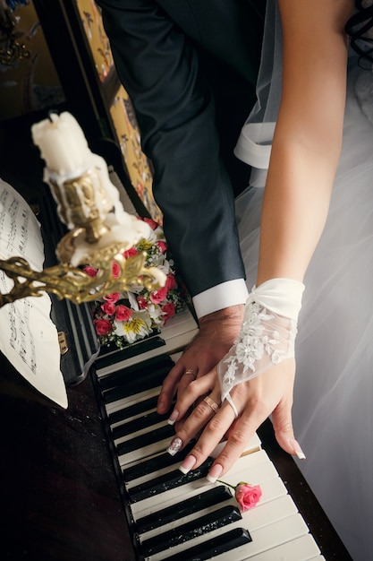 Photo hands of married man and woman with wedding rings laying on keys of piano with beige roses nearly