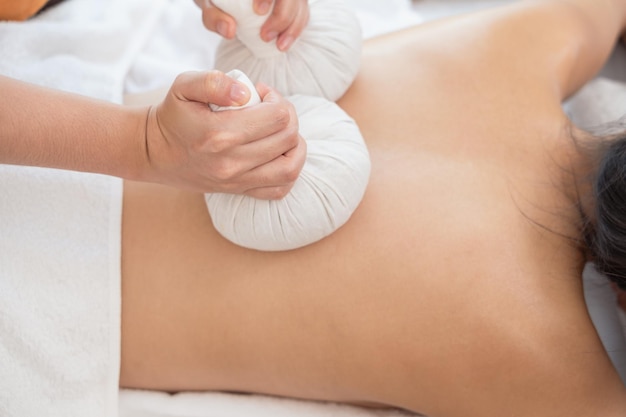 Hands of masseur massaging back of young woman with with herb pouches on massage table