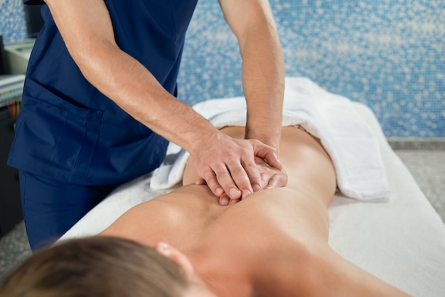 Hands of masseur stretching spine of female client in spa