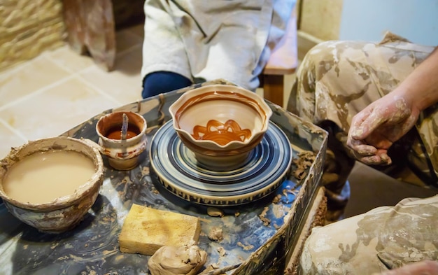 The Hands of a master and a student make a pitcher on a Potters wheel of yellow clay Selective focus on hands