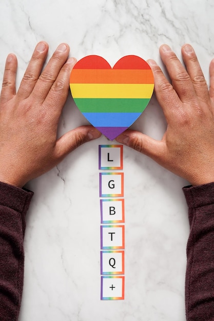 Hands of a mature man placing a heart with the colors of the movement over the acronym LGBTQ