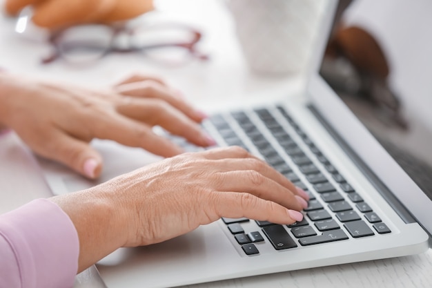 Hands of mature woman working on laptop at home