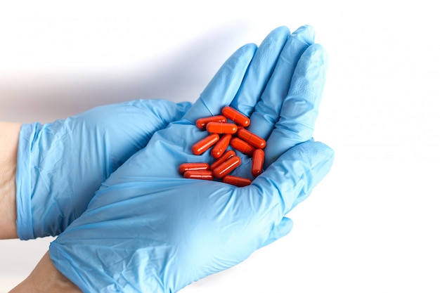 Hands in medical gloves hold a handful of red pills. Blue disposable gloves isolated. Pharmaceutical concept. the medicine