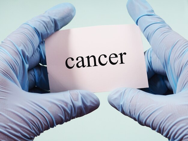 Photo hands in medical gloves hold a sign with the inscription cancer