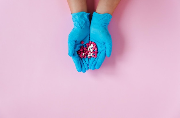 Hands in medical gloves with pills Pink background Medical concept top view space for text