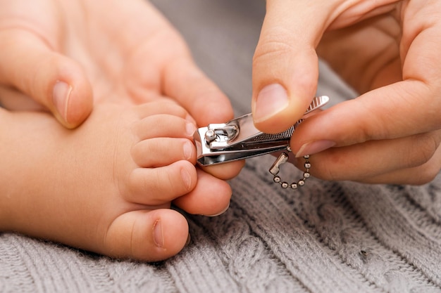 Hands of a mother cutting nails on the bare foot of a baby, close-up. Selective focus