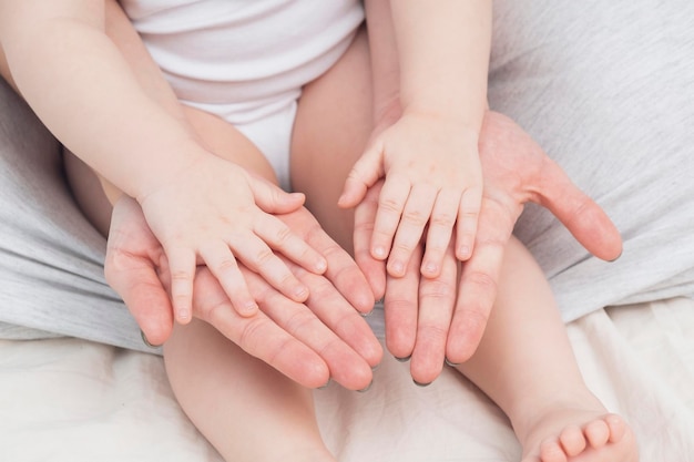 Hands of a mother and a small child closeup light colors Mom hugs the baby The concept of maternal parental love and care Background for Mothers Day and childs Day