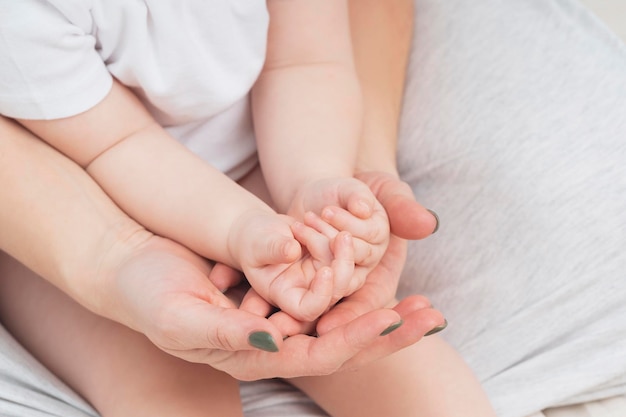 Hands of a mother and a small child closeup light colors Mom hugs the baby The concept of maternal parental love and care Background for Mothers Day and childs Day