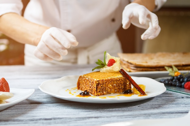 Hands near plate with cake. Cake with decoration on plate. Honey cake and cinnamon stick. Traditional recipe and new design.