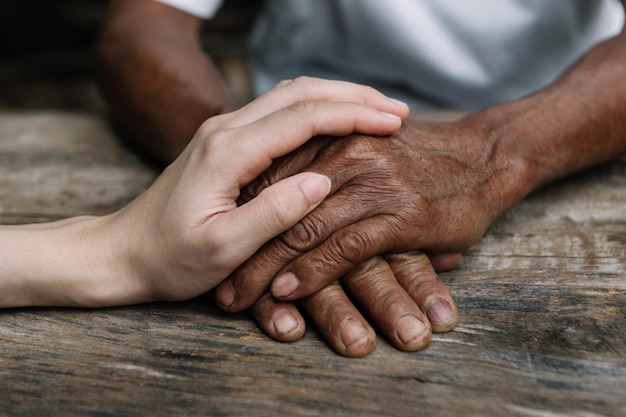 Hands of the old man and a woman hand on the wood table in sun light