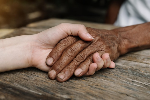 Hands of the old man and a woman hand on the wood table