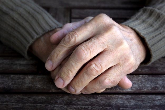 Photo hands of old senior man with wrinkled palm on wooden table.