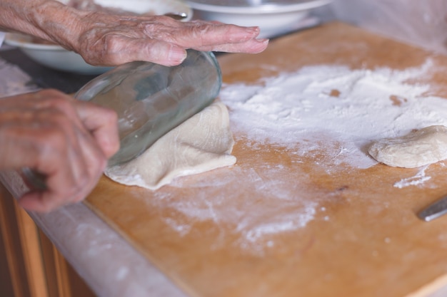 Hands of old woman on flattened dough.