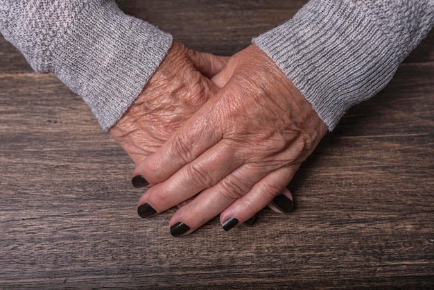 Hands of an old woman resting on a wooden table