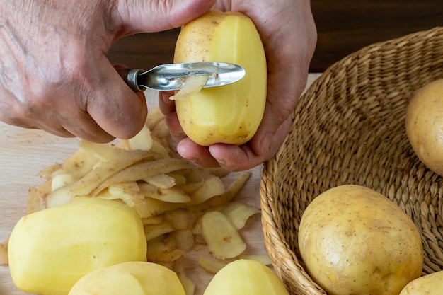 Hands peel potato peelings on wooden cutting board