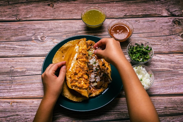 Hands of a person preparing a gringa pastor a la diabla accompanied by sauces and other condiments