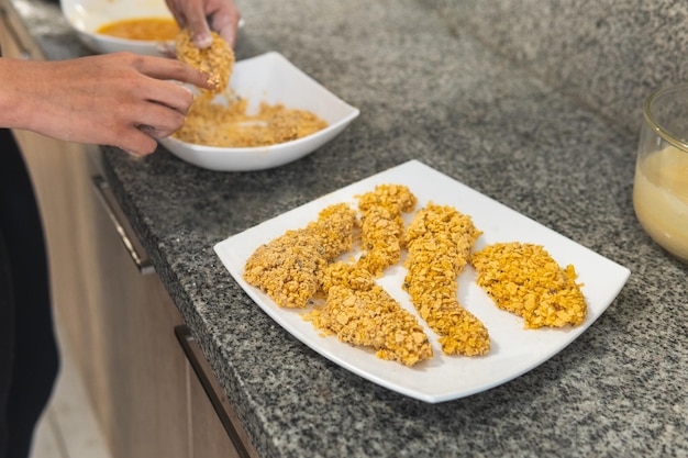 Hands preparing fried chicken in batter with cereal