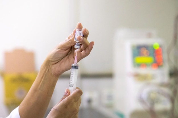 Hands preparing injection for vaccine or treatments with dialysis equipment in the background