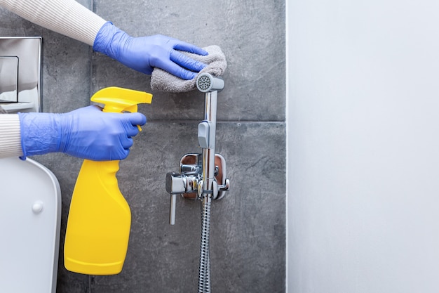 Hands in protective gloves cleaning hygienic shower in sanitary room