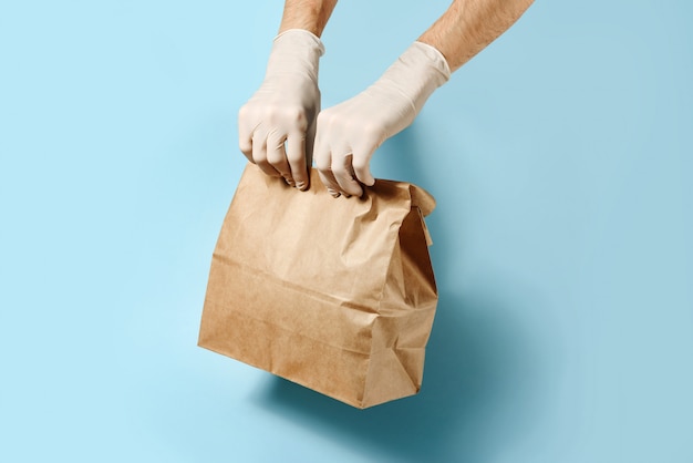 Hands in protective gloves hold craft package on a blue wall with a copy space.