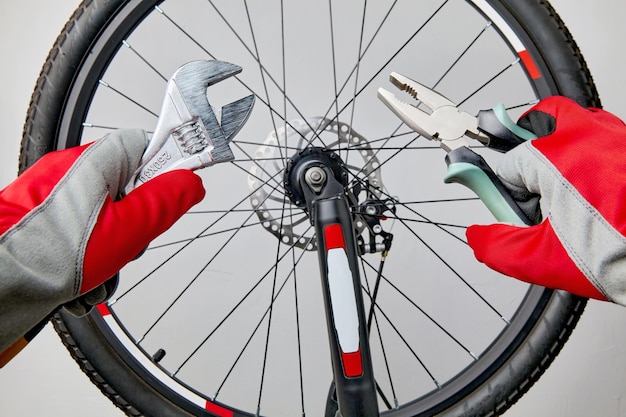 Hands in protective gloves with adjustable wrenches and pliers on the background of a bicycle wheel