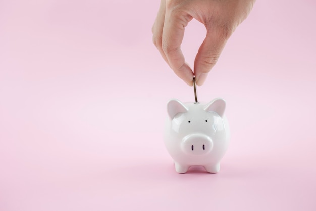 Hands put money coin into piggy bank on pink background for saving money wealth