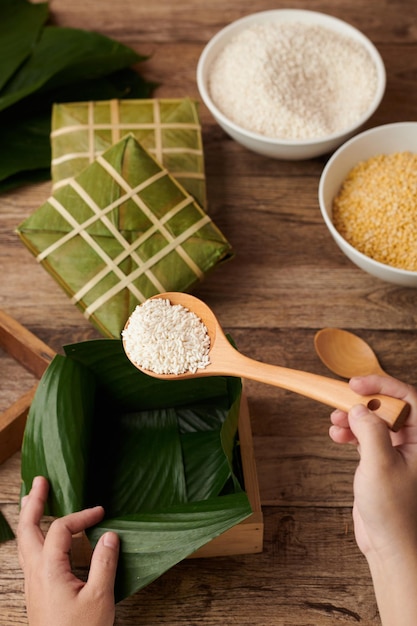 Hands putting white rice in box lined with lotus leaves when making sticky rice cake