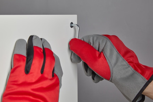 Hands in red gloves twist the confirmat with a hexagon key