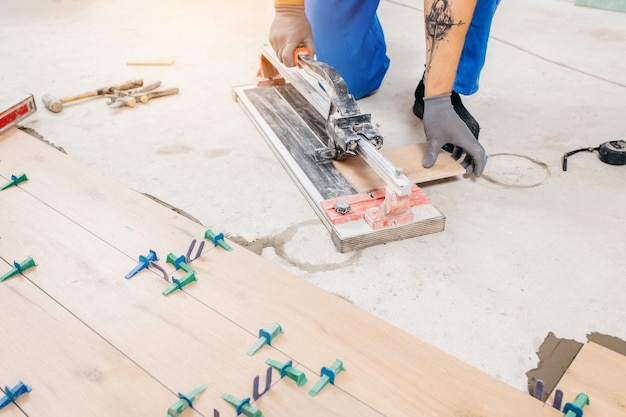 Hands of repairman cut ceramic tiles at tile cutter on the floor. Close up