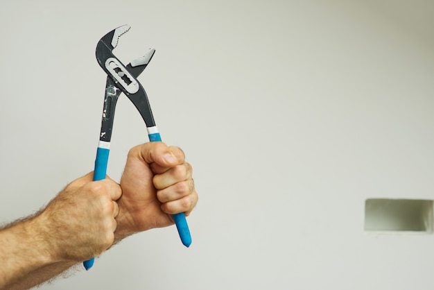 Photo hands of repairman holding a pipe wrench with blue handle over white background