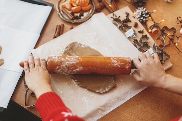 Hands rolling raw gingerbread dough with rolling pin on rustic table Making Christmas cookies