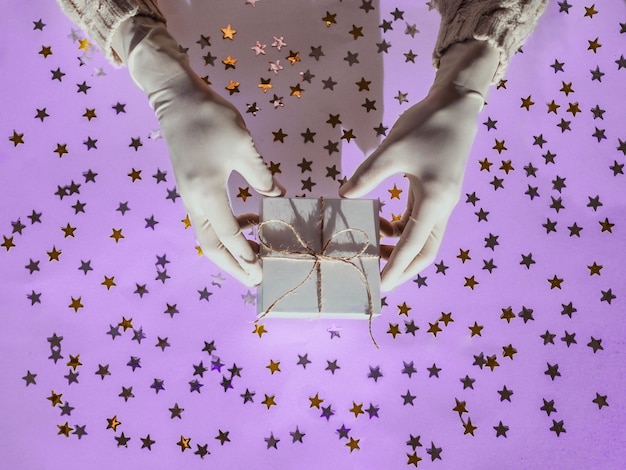 Photo hands in rubber protective gloves hold a white gift box golden and silver confetti stars