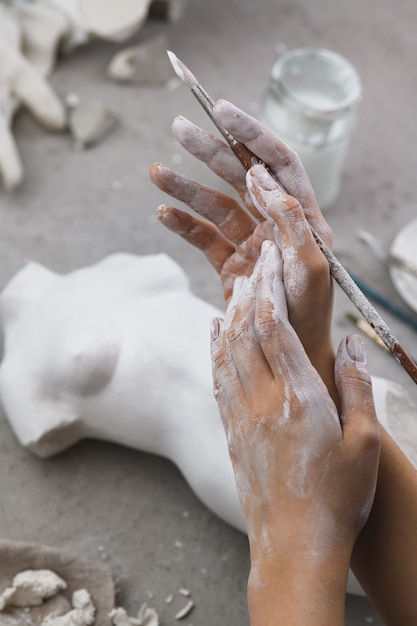 Hands of a sculptor in plaster with a brush