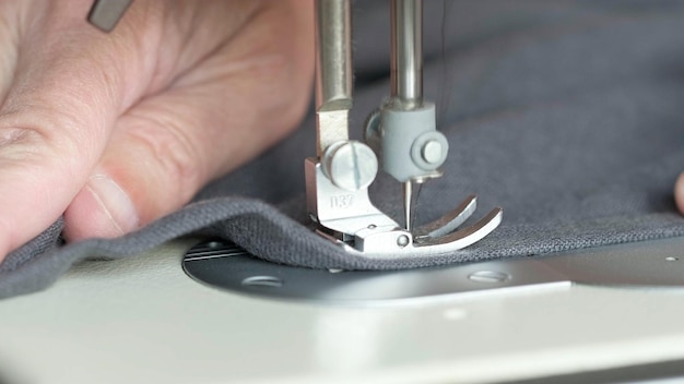 Hands of seamstress sewing with a professional machine embroiders sews on grey fabric