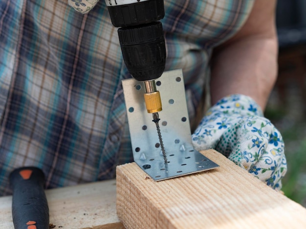 Hands of senior woman assembles a wooden frame of building using metal fasteners using a screwdriver