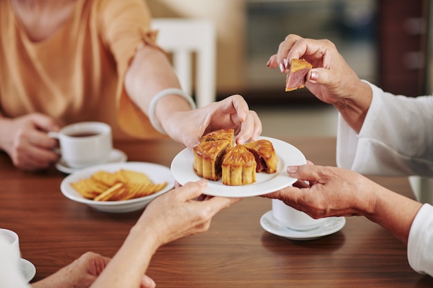 Hands of senior women eating delicious traditional moon cake when celebrating mid autumn festival at home